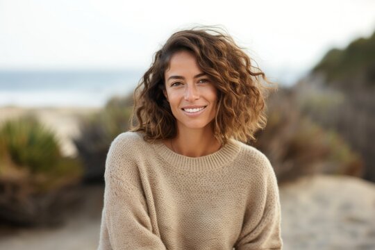 medium shot portrait of a Israeli woman in her 30s wearing a cozy sweater against a beach background