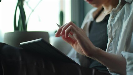 Woman artist drawing on tablet. Creative girl holding notepad with digital pencil in hands and working remotely from home. Freelancer using computer to create art sitting near window