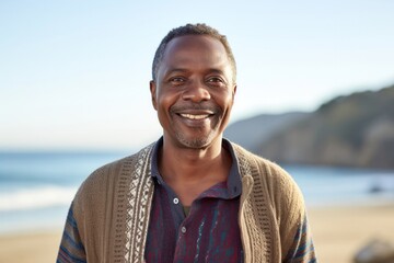 medium shot portrait of a Kenyan man in his 50s wearing a chic cardigan against a beach background - obrazy, fototapety, plakaty