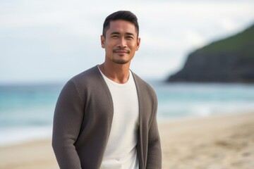 medium shot portrait of a confident Filipino man in his 30s wearing a chic cardigan against a beach background