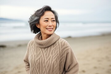 medium shot portrait of a confident Japanese woman in her 40s wearing a cozy sweater against a beach background