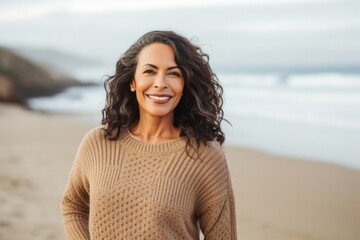 portrait of a Mexican woman in her 50s wearing a cozy sweater against a beach background