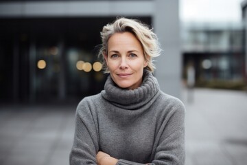 portrait of a Polish woman in her 40s wearing a cozy sweater against a modern architectural background