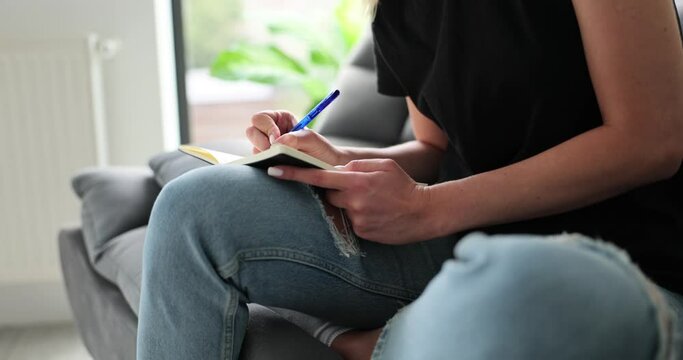 Woman hands write notes in diary at home on sofa closeup. Making notes and diary concept