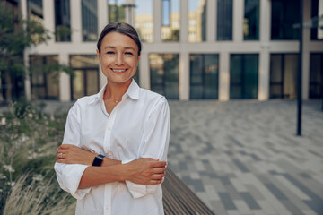 Portrait of smiling business woman standing on modern office building background and looks camera