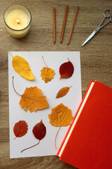 Naklejka na ściany i meble Paper with pressed colorful leaves, book, scissors, pencils, picture frame, scented candle and decorative pumpkin on the table. Making autumnal themed herbarium at home. Top view.