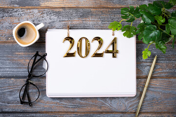 New year resolutions 2024 on desk. 2024 goals list with notebook, coffee cup, plant on wooden...