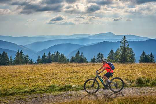 nice senior woman on her electric mountain bike cycling on Feldberg summit with stunning view over the Black Forest mountains and valleys, Baden-Wuerttemberg Germany