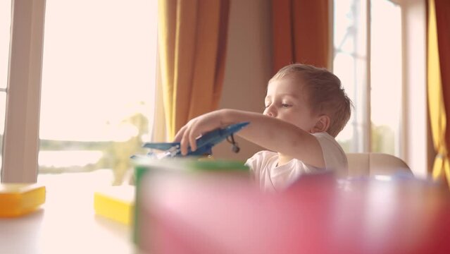 child baby playing with toys airplane car. happy family kid dream concept. child son on the table near the window plays a toy plane car lifestyle cubes the glare of the sun from the window