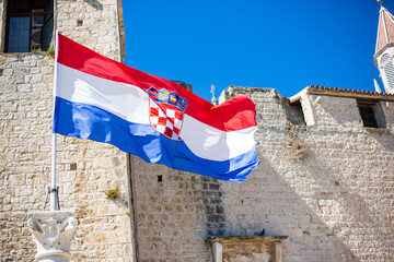 A croatian flag waving in the wind in front of old, white brick wall. Croatia is a popular tourist...
