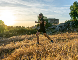 Middle-aged trail runner with gray hair sprinting through a golden field at sunset.