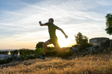 Middle-aged trail runner with gray hair leaping at sunset.