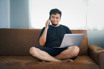 People And Technology. Portrait Of Smiling Asian Man Holding And  Tablet Sitting On Couch Indoors In Living Room. 

