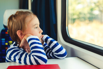 Cute child looking out the train window. Little boy is traveling on the train. Kid travels on a train.