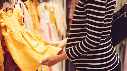 Pregnant woman choosing dress and bodysuits at clothing store. Baby fashion, shopping time, sale and pregnancy concept.