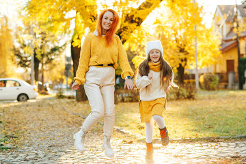 Happy family enjoying autumn weather in the park. Lovely girl with her mom having fun on the walk.