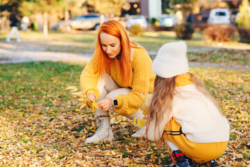 Mother and child girl playing with autumn leaves. Happy family enjoying autumn day together.