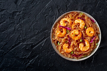 Konjac pasta. Shirataki fettuccine with shrimps and vegetables, a healthy diet dish, overhead flat lay shot on a black table with a place for text