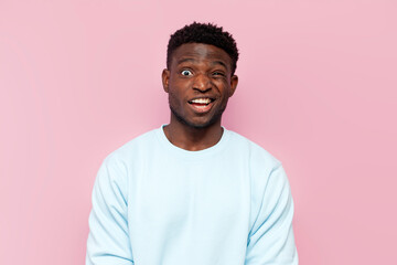 puzzled african american man in blue sweater in amazement on pink isolated background, confused and stunned man - obrazy, fototapety, plakaty