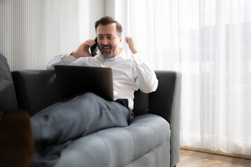 Businessman using laptop and talking on the phone while sitting on sofa at home