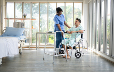Young female nurse helping young male patient to walk on walker at patient room of hospital