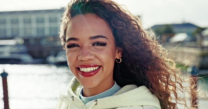 Face, smile and wind with a black woman in the harbor for style, cosmetics or clothing. Portrait, water and young model or influencer on the pier for luxury makeup or beauty with a summer breeze