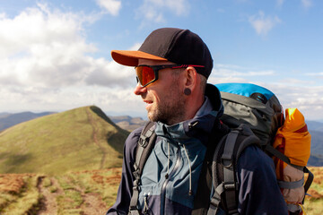 man in jacket and sunglasses stands on the mountain and looks at the sun, tourist guy in mountain...