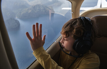 Curious boy looking out airplane window flying above sea