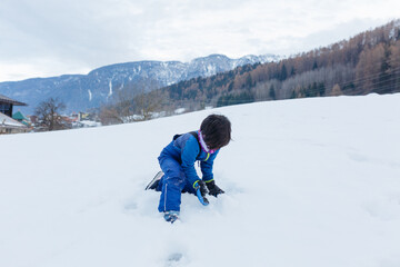 Fototapeta na wymiar sitting in blue winter clothes child playing with the snow on the hill
