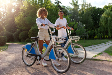 african american couple walking in the park with bicycles and talking, man and woman together with eco transport