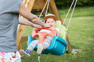 Fototapeta na wymiar Mother pushing her infant baby boy child on a swing on playground outdoors