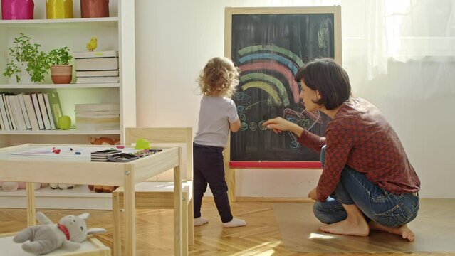 Mother and child drawing together on chalk board at home. 