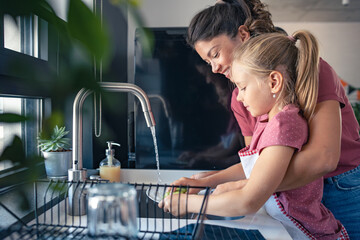 A cute little girl helps her mother wash dishes. Child doing house chores. Mother teaches a child to wash dishes. - 649781837