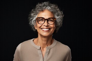 Confident, smiling mature woman with curly hair and glasses on black background - Powered by Adobe
