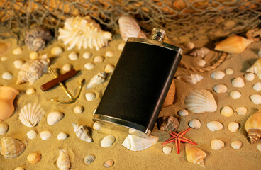 Black flask on sand among shells and stones.		