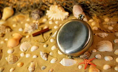Steel flask on sand among shells and stones.