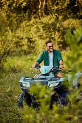 A smiling man driving a quad bike through the forest, enjoying the adventure.