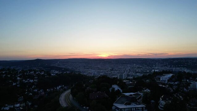 In diesem atemberaubenden Drohnenshot fliegt die Kamera &uuml;ber Stuttgart, w&auml;hrend der Himmel sich in ein magisches Lila verwandelt und die Sonne am Horizont untergeht.