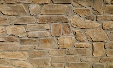 Rustic stone wall with brown rocks of different shapes and sizes on concrete. Background and...