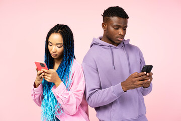Couple of serious African American friends holding mobile phones, communication online isolated on pink background. Technology, social media addiction concept