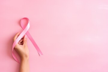 Hand holding pink ribbon for supporting people living and illness on pink background. October breast cancer awareness month, world cancer day, national cancer survivor day. Healthcare medical concept