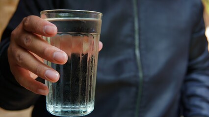 hand with glass of water. someone in a black jacket is serving a glass of fresh water
