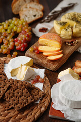 Variety of delicious dishes on a wooden table. The focus is on the round wheel of white cheese in the center. 3 types of cheese, grapes, bread, crackers on a wooden table. medium shot, vertical frame