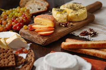three different cheeses on a wooden table with grapes, bread and crackers. brie cheese, camembert, cheddar on the table. wooden table background. the middle plan.