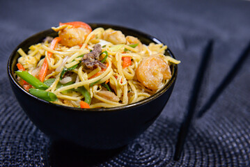 mixed fried noodles with with chicken, carrot, spring onion, bell pepper, egg and chopsticks served in bowl side view of chinese food