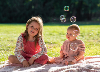 Portrait of sisters. A sweet, smiling girl of 5 years old, her younger sister, one year old, is...