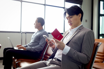 Passengers wait for flight, Asian businessman sits at departure terminal airport, holds mobile phone and passport for checking information, travel on holiday vacation or business trip transportation.