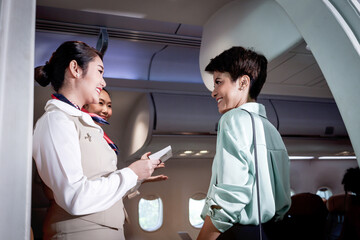 Beautiful Asian female air hostess standing at airplane entrance gate, flight attendant woman welcome and check passenger before boarding, cabin crew work in airplane, traveling Airline transportation