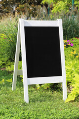 Vintage wedding black chalkboard mockup stand, easel with welcome sign decorated, outdoors, in a park with flowers and plants.