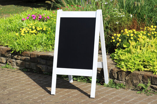 Vintage wedding black chalkboard mockup stand, easel with welcome sign decorated, outdoors, in a park with flowers and plants.